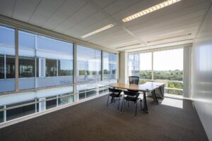 Modern kantoor met hoekbureau en vergaderstoelen aan de Thomas R. Malthusstraat met uitzicht op een groene omgeving.
